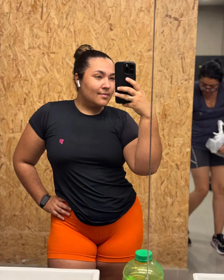Luzia de camiseta preta e short laranja no espelho, antes do acompanhamento
