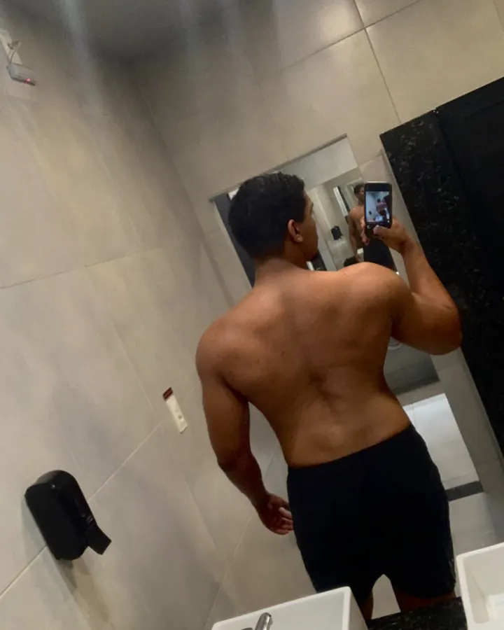 Abimael de costas no espelho da academia, depois do acompanhamento, com costas e ombros mais desenvolvidos