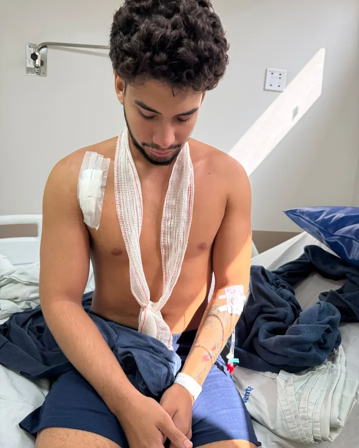 Paulo Henrique sentado na cama do hospital, com o ombro direito imobilizado após a cirurgia
